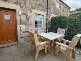 An outdoor seating area with a wooden table and chairs at Heather Cottages - Grayling in Bamburgh