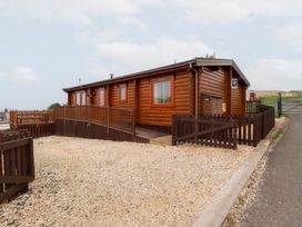 A log cabin with a wooden fence and gravel driveway at Heather Cottages - Grey Heron in Bamburgh