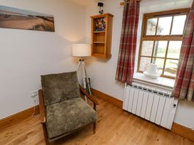 A living room with a chair, lamp, and window at Heather Cottages - Grey Seal in Bamburgh