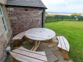 A round wooden table with benches outside at Heather Cottages - Grey Seal in Bamburgh