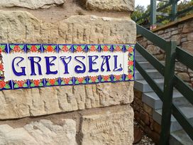 A sign reading GREY SEAL attached to a stone wall near a staircase at Heather Cottages - Grey Seal in Bamburgh