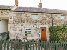 An outdoor area with a wooden table and chairs near the entrance at Heather Cottages - Plover in Bamburgh