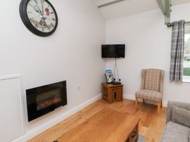 A living room with a wall clock, fireplace, television, armchair, and coffee table at Chiff Chaff in Lucker