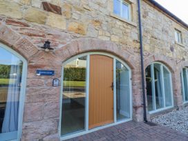 An exterior view of Goldfinch Cottage with a stone wall and an orange front door at Goldfinch in Lucker