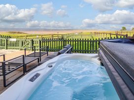 A hot tub on a patio with deck chairs and a view of the garden at Pipistrelle in Bamburgh