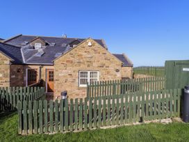 An outdoor area with a stone house and a green fence at Goosander in Bamburgh