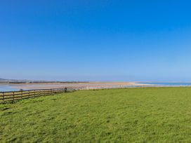 A grassy area with a fence and water under a clear blue sky at Jackdaw in Bamburgh