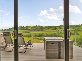 A balcony with chairs and a table overlooking green hills at Bwncath Garthmyl