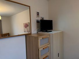 A wooden dresser with three drawers and a small television on a white cabinet next to a wall with three framed pictures and a large mirror