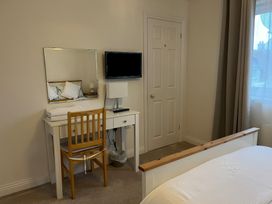 A bedroom with a wooden chair at a white desk with a mirror and a TV mounted on the wall at Cliffwalk Cottage in Southwell