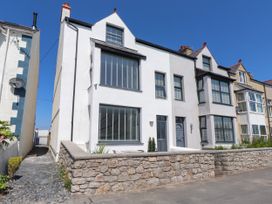 A house with multiple windows and a stone wall in front at Ty Haul in Rhosneigr