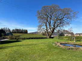A garden with a tree, grass, pond, and buildings at How Hill Farm Cottage in Greystoke