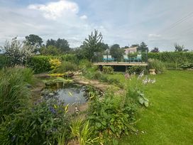 A garden with a pond and a deck with chairs at How Hill Farm Cottage Greystoke