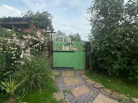A green gate surrounded by flowers and plants at How Hill Farm Cottage in Greystoke