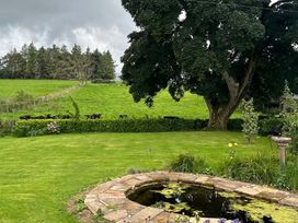 A garden with a pond and cows in a field at How Hill Farm Cottage in Greystoke