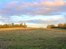 A field with grass and cut crops with trees in the background under a cloudy sky