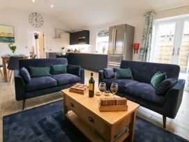 A living room with two navy sofas a wooden coffee table with wine glasses and a bottle and a kitchen with appliances in the background at Bracken Cottage in Pocklington