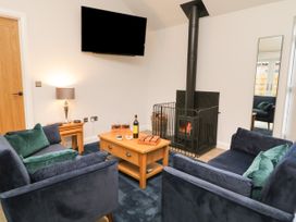 A living room with blue sofas green cushions a wood stove a wooden coffee table with wine and snacks a lamp two nesting tables and a wall-mounted TV at Bracken Cottage in Pocklington