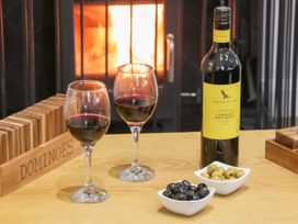 A wooden table with two glasses of red wine a bottle of red wine two bowls of olives and a dominoes set in front of a fireplace at Bracken Cottage in Pocklington