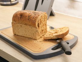 A sliced loaf of seeded bread on a cutting board with a bread knife in a kitchen