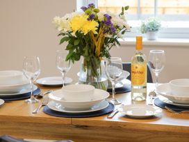 A dining table set with white plates bowls wine glasses cutlery a bottle of white wine and a vase of mixed flowers at Bracken Cottage in Pocklington