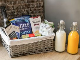 A wicker basket with champagne chocolate crisps biscuits coffee and tea next to bottles of milk and orange juice on a wooden surface at Bracken Cottage in Pocklington