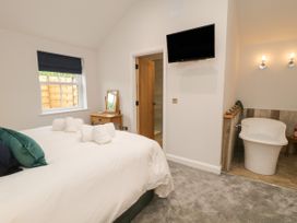 A bedroom with a bed with towels on it a wooden desk with a mirror a wall-mounted television and a bathtub area at Bracken Cottage in Pocklington