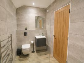 A bathroom with a wall-mounted toilet a sink with a mirror a wooden door and a heated towel rail at Bracken Cottage in Pocklington