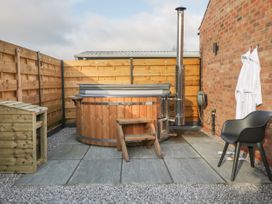 An outdoor patio area with a wooden hot tub a small wooden step a black chair two white robes hanging on a brick wall and wooden fencing at Bracken Cottage in Pocklington