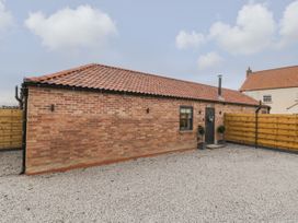 A brick building with a tiled roof and a small window next to a door with plants outside surrounded by a wooden fence at Bracken Cottage in Pocklington