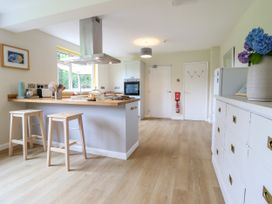 A kitchen with wooden stools, a kitchen island, oven, cabinet, and a white dresser with flowers at The Wardens House in Tregynon near Newtown