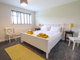 A bedroom with a white bed with yellow towels on it two white chairs two black bedside tables with yellow lamps and a yellow rug on the grey carpet at The Wardens House in Tregynon near Newtown