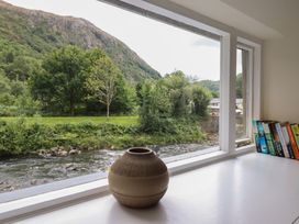A window with a vase and books overlooking a river at Riverside Cottage Beddgelert