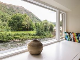 A window with a vase and books overlooking a river at Riverside Cottage in Beddgelert