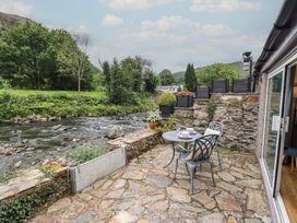 An outdoor seating area with a table and chairs by a river at Riverside Cottage in Beddgelert