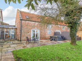 A brick house with a tiled roof a stone patio with a table and chairs a hot tub and a tree in the garden at Servant's Quarters in Bolton Percy near Tadcaster