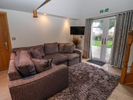 A living room with a sectional sofa a wall-mounted TV and glass doors leading outside at Servant's Quarters Bolton Percy near Tadcaster