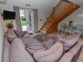A living room with a large gray sofa a wooden staircase a small round table with chairs and glass doors leading outside at Servant's Quarters Bolton Percy near Tadcaster