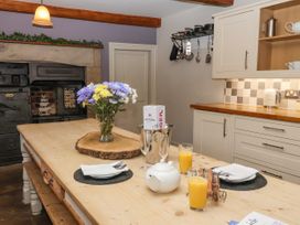 A kitchen with a wooden table set with two glasses of orange juice a teapot plates and cutlery a vintage stove and cream cabinets at Servant's Quarters Bolton Percy near Tadcaster