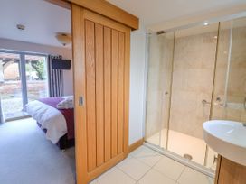 A bedroom with a bed and television partially visible through a wooden sliding door next to a bathroom with a shower and sink at Servant's Quarters Bolton Percy near Tadcaster