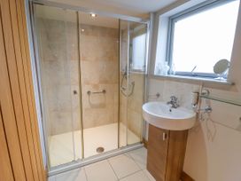 A bathroom with a glass-enclosed shower and a sink with a wooden cabinet beneath a window at Servant's Quarters in Bolton Percy near Tadcaster