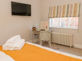 A bedroom with a bed covered by an orange blanket and white towels a desk with a chair and a tri-fold mirror under a window and a wall-mounted TV at Servant's Quarters Bolton Percy near Tadcaster