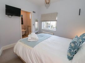 A bedroom with a bed pillows and folded towels with a wall mounted tv and an open door to a bathroom at Servant's Quarters in Bolton Percy near Tadcaster