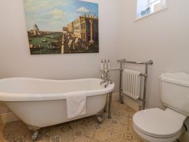 A bathroom with a clawfoot bathtub a toilet a radiator and a painting of a canal scene on the wall at Servant's Quarters Bolton Percy near Tadcaster
