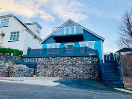 A blue house with a stone retaining wall and a balcony above a street at Ingledene in Brixham