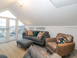 A sitting room with a gray sofa with cushions a brown armchair with a cushion a gray ottoman a floor lamp glass doors and a balcony at Ingledene in Brixham