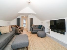 A living room with gray sofas a brown armchair a large TV on the wall and a woven rug at Ingledene in Brixham