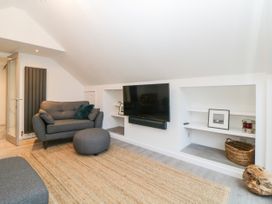 A living room with grey sofa and ottoman a mounted TV and shelving with baskets and picture frames at Ingledene in Brixham