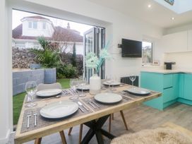 A dining table set with plates and glasses next to an open door leading to a garden in a kitchen with turquoise cabinets at Ingledene in Brixham