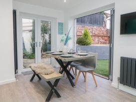 A dining area with a wooden table set with plates and glasses chairs and a bench near glass doors and a window at Ingledene in Brixham